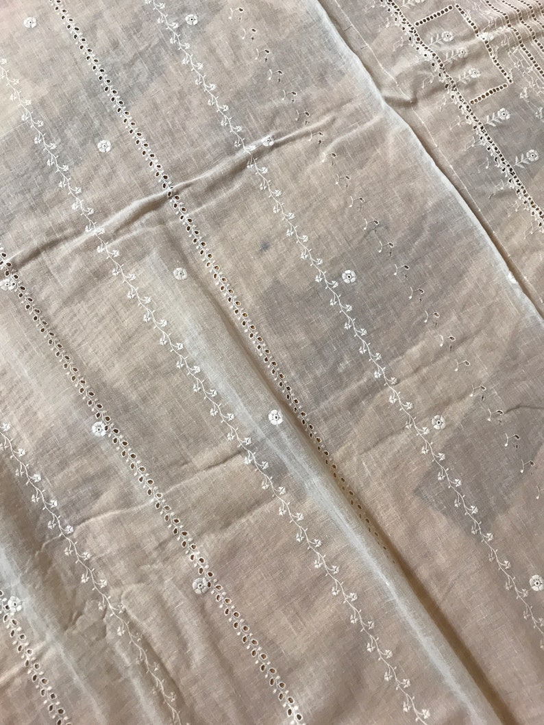 May include: White cotton fabric with a delicate embroidered pattern of small flowers and vines. The fabric has a sheer, lightweight texture and is perfect for crafting or sewing projects.