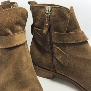 May include: A pair of brown suede ankle boots with a zipper on the side and a strap across the top.