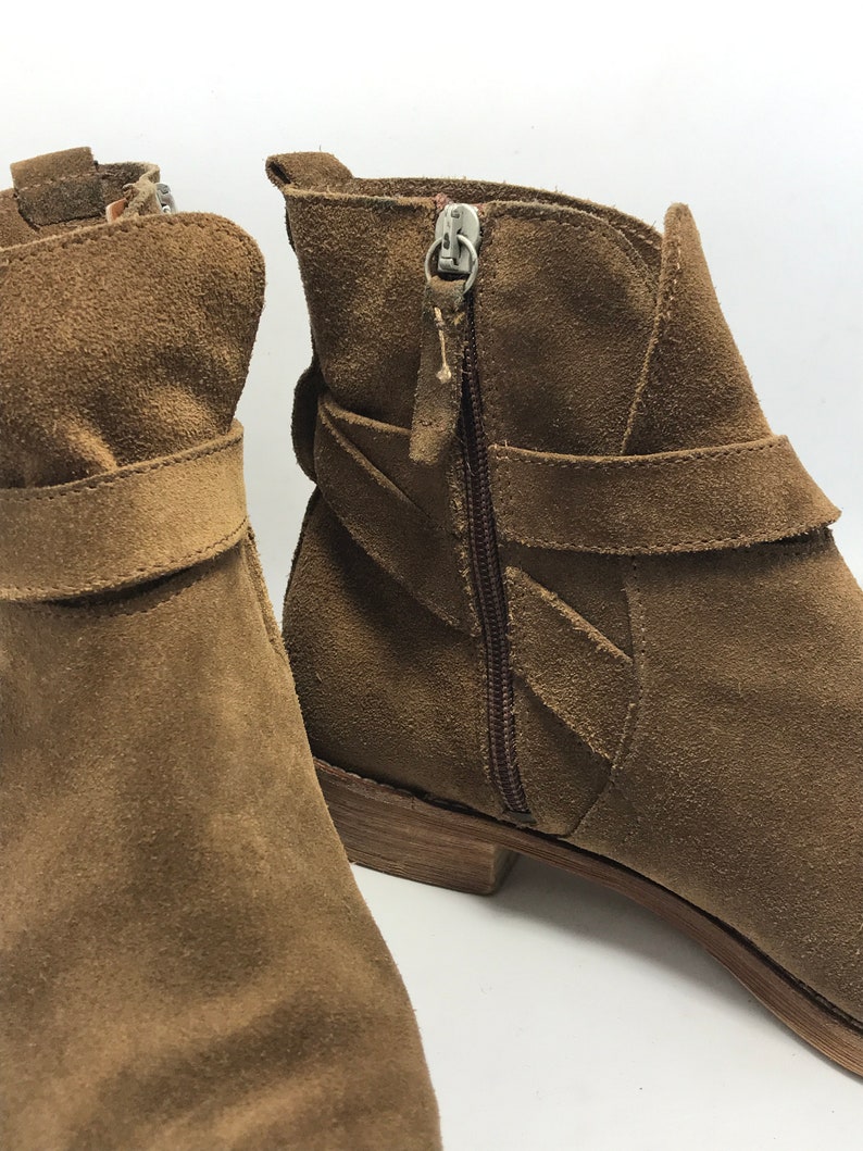 May include: A pair of brown suede ankle boots with a zipper on the side and a strap across the top.