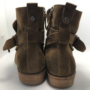 May include: A pair of brown suede ankle boots with buckle accents and side zippers. The boots have a wooden heel and a brown leather sole.