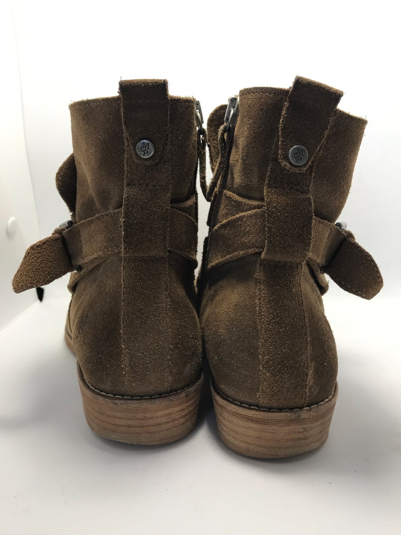 May include: A pair of brown suede ankle boots with buckle accents and side zippers. The boots have a wooden heel and a brown leather sole.
