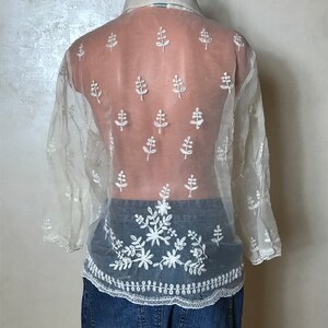 May include: A white sheer blouse with embroidered floral details. The blouse has a collared neckline and long sleeves. The embroidery is in a delicate floral pattern.