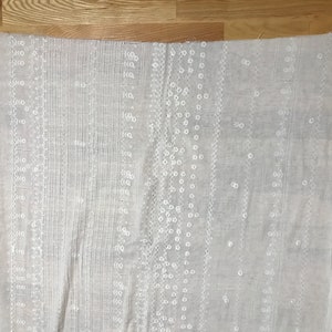 May include: White cotton fabric with an embroidered pattern of small white circles and lines. The fabric is lightweight and sheer.
