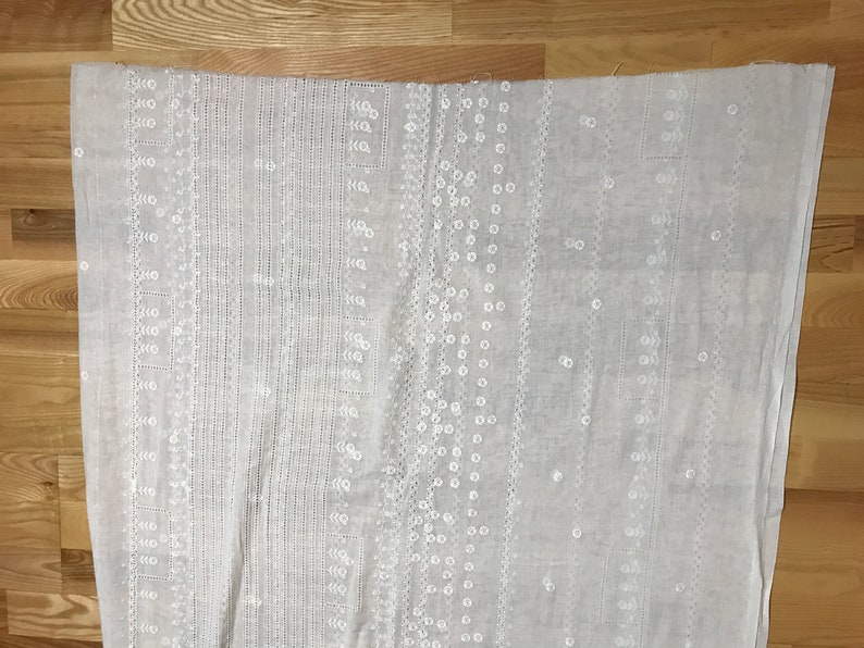 May include: White cotton fabric with an embroidered pattern of small white circles and lines. The fabric is lightweight and sheer.