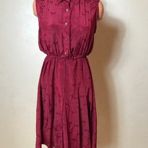 May include: A burgundy sleeveless dress with a collared neckline and button closure. The dress has a fitted bodice and a flowing skirt with a small bow pattern.