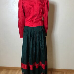 May include: A red long-sleeved blouse with a green skirt. The skirt has a red band at the bottom and black lace trim.