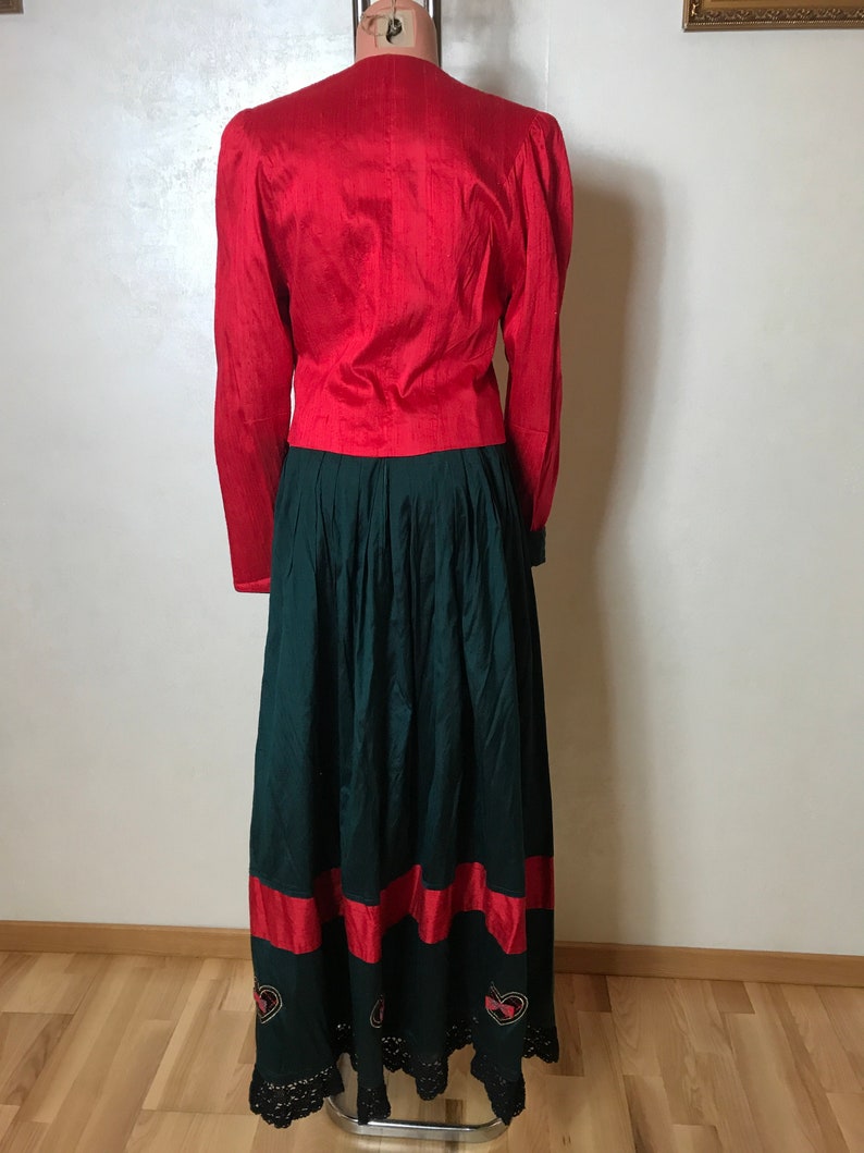 May include: A red long-sleeved blouse with a green skirt. The skirt has a red band at the bottom and black lace trim.
