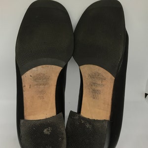 May include: Black leather shoes with a low heel. The soles are black rubber with a textured pattern. The shoes are labelled "6 1/2 EU 9 US".