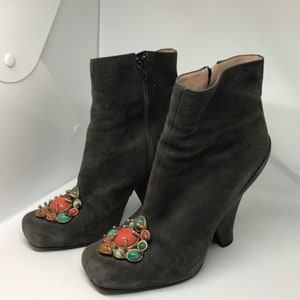 May include: A pair of gray suede ankle boots with a chunky heel and jeweled embellishments. The embellishments are made of gold metal and colorful stones.