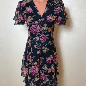 May include: A navy blue floral dress with a V-neckline and short sleeves. The dress has a ruffled hem and a button-up front.