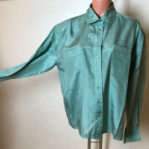 Op de afbeelding: Een lang mouwig, lichtgroen zijden overhemd met een kraag en knoopsluiting. Het overhemd heeft twee opgestikte zakken aan de voorkant en een licht oversized pasvorm.