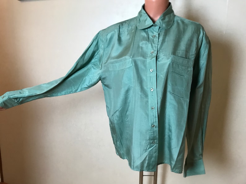 Op de afbeelding: Een lang mouwig, lichtgroen zijden overhemd met een kraag en knoopsluiting. Het overhemd heeft twee opgestikte zakken aan de voorkant en een licht oversized pasvorm.