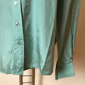 Op de afbeelding: Een lichtgroen overhemd met lange mouwen, een knoopsluiting en een enkele knoopmanchet aan elke mouw.