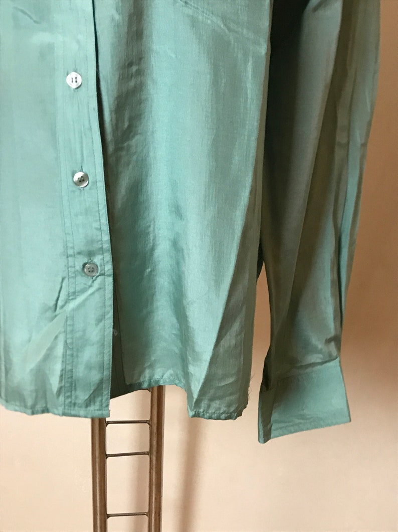 Op de afbeelding: Een lichtgroen overhemd met lange mouwen, een knoopsluiting en een enkele knoopmanchet aan elke mouw.