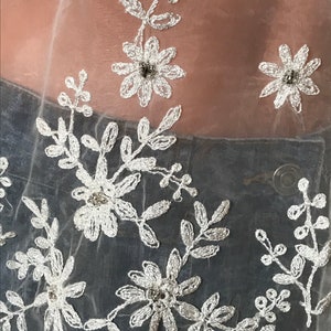May include: White sheer fabric with delicate floral embroidery and small silver beads.