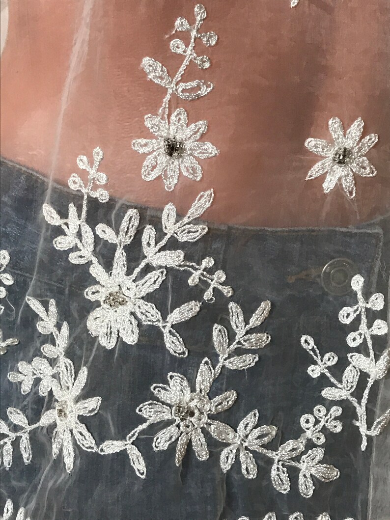 May include: White sheer fabric with delicate floral embroidery and small silver beads.