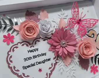 May include: A handmade birthday card with a white background and a decorative arrangement of paper flowers in shades of pink, white, and silver. The card features a heart-shaped element with the text "Happy 30th Birthday Special Daughter."