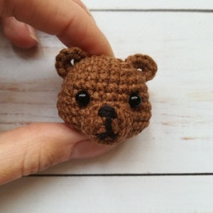 May include: A brown crocheted bear head with black eyes and a black nose.