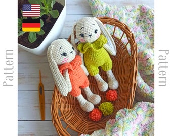 May include: Two crocheted bunny amigurumi toys in a wicker basket. One bunny is wearing an orange outfit and the other is wearing a green outfit. Both bunnies have white yarn for their ears and bodies.