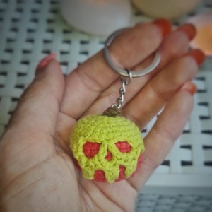 May include: A green and red crocheted apple keychain with a skull design.