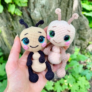 Pu&ograve; includere: Due giocattoli amigurumi all'uncinetto a forma di formiche. Una formica &egrave; rosa con gli occhi verdi e l'altra &egrave; beige con gli occhi neri. Entrambe le formiche hanno gambe e antenne nere.