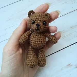 May include: A small brown crocheted teddy bear with black eyes and a brown nose.