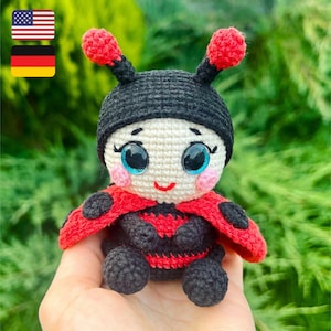 May include: A crocheted ladybug doll with black and red accents, big blue eyes, and a sweet smile. The doll is sitting on a hand with a green background.