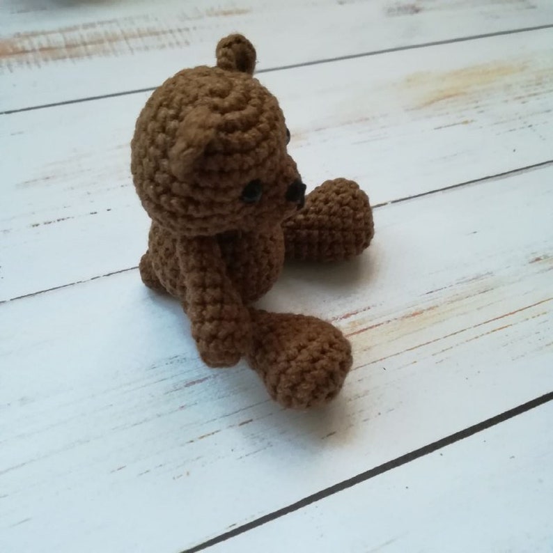 May include: A small brown crocheted teddy bear sitting on a white wooden surface.