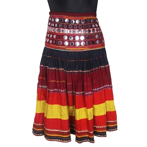 May include: A long, multi-colored skirt with a wide waistband decorated with small round mirrors. The skirt has a layered design with alternating bands of red, yellow, and black fabric.