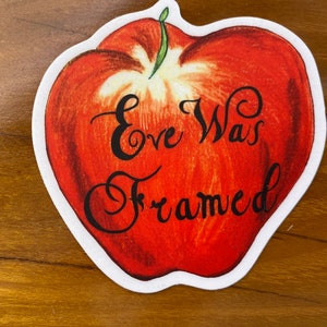 May include: A red apple sticker with the text "Eve Was Framed" in black cursive lettering.