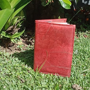 Op de afbeelding: Een rood lederen gebonden dagboek met een textuur op de kaft ligt op een bed van groen gras.