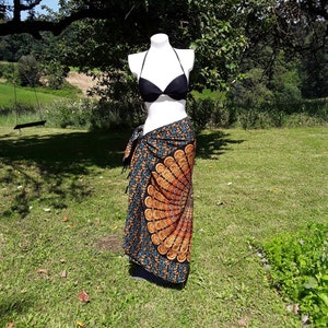 Pode incluir: Um top de biquíni preto com um sarong colorido com um design de mandala. O sarong é amarrado na cintura e tem um detalhe de franjas.