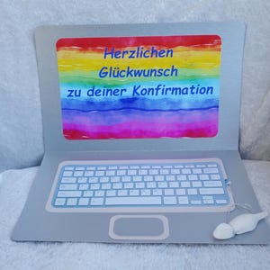 Könnte beinhalten: Ein silberner Laptop mit einem Regenbogen-Aquarellhintergrund auf dem Bildschirm. Der Bildschirm zeigt den Text "Herzlichen Glückwunsch zu deiner Konfirmation".
