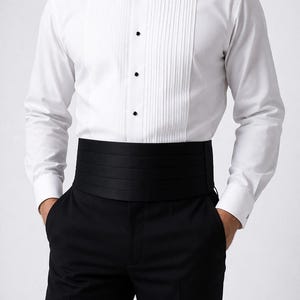 May include: A formal white dress shirt with a pleated front, black bow tie, and black buttons. The outfit includes black trousers and a black cummerbund. The shirt has long sleeves and buttoned cuffs. The overall look is classic and elegant.