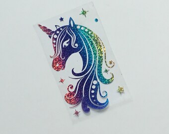 May include: A holographic unicorn sticker with a rainbow mane and horn. The unicorn's head is detailed with a glittery finish, transitioning from red to blue and green. Small star-shaped stickers are scattered around the unicorn.