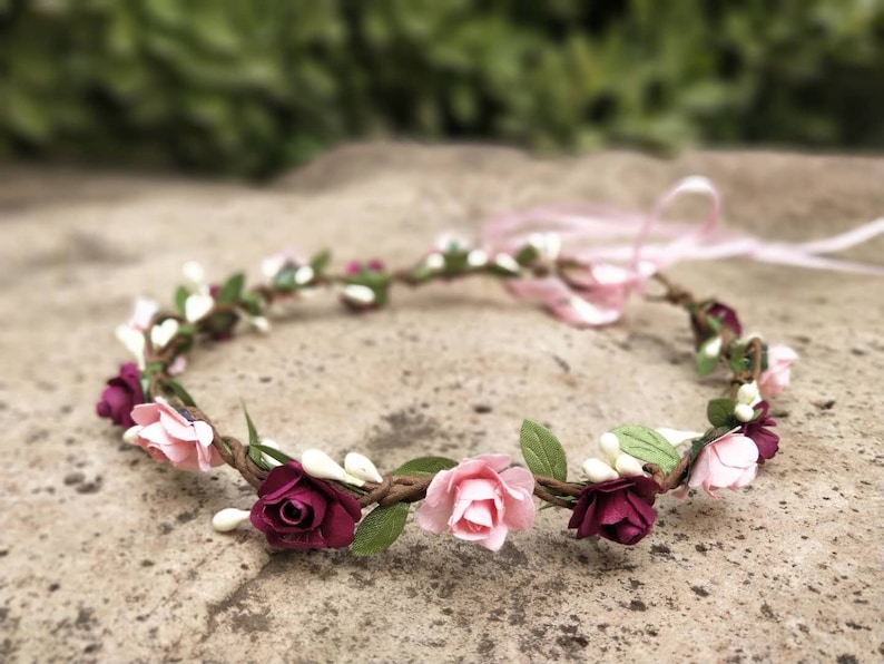 Puede incluir: Una corona de flores con flores rosas y burdeos y hojas verdes. La corona est&aacute; hecha de una base de alambre marr&oacute;n.