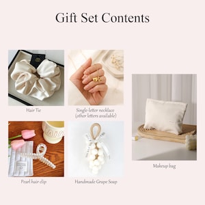 May include: A gift set with various items, including a cream-colored scrunchie, a single-letter necklace, a pearl hair clip, a handmade grape soap, and a makeup bag. The text "Gift Set Contents" is at the top. The makeup bag is on a wooden tray.