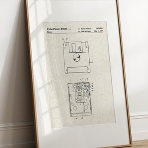 May include: Framed patent print of a 8.89 cm floppy disk, with detailed technical drawings in black ink on a beige background. The frame is a light brown colour, and the print is titled "United States Patent". The patent number and date are also visible.
