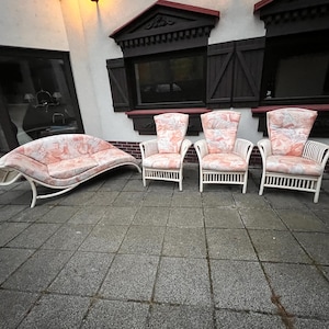 Può includere: Un set di quattro mobili da giardino in vimini bianco con cuscini a fiori rosa. Il set comprende tre sedie e una chaise longue curva.