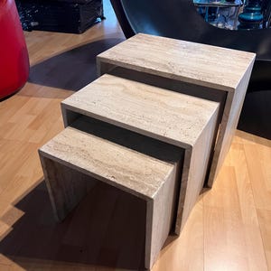 Könnte beinhalten: Satz von drei Beistelltischen mit hellbeigem, steinähnlichem Aussehen. Die Tische sind rechteckig und lassen sich platzsparend stapeln. Der größte Tisch ist etwa 61 cm breit, 46 cm tief und 46 cm hoch.