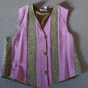 Könnte beinhalten: Eine Vintage-Weste in Rosa- und Grüntönen. Die Weste hat einen V-Ausschnitt und drei dekorative Knöpfe. Die Vorderteile sind rosa, mit grünen, tweedartigen Streifen auf der Vorderseite. Das Innenfutter ist dunkelolivgrün.