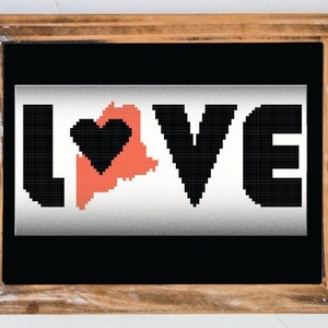 May include: A framed sign with the word "LOVE" in black pixelated letters. The letter "O" is replaced with the outline of the state of Maine in red, with a black heart inside.