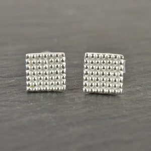Könnte beinhalten: Ein Paar silberne quadratische Ohrstecker mit einer strukturierten Oberfläche.