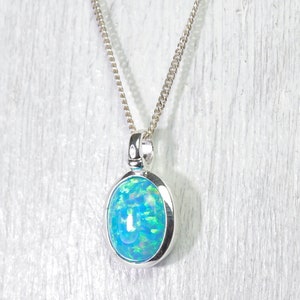 Könnte beinhalten: Eine silberne Kettenkette mit einem Anhänger mit einem blauen Opal-Edelstein, der in einer silbernen Fassung gefasst ist.