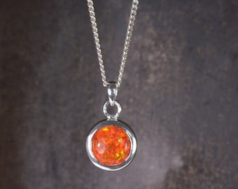 Può includere: Una collana con catena d'argento con un ciondolo rotondo con una pietra preziosa di opale arancione brillante.