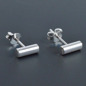 May include: A pair of silver stud earrings with a small, rectangular bar. The earrings have a simple, minimalist design.