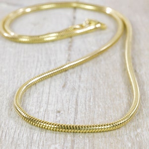 Op de afbeelding: Een gouden slangenketting. De ketting is gemaakt van kleine, in elkaar grijpende schakels die een gladde, vloeiende uitstraling creëren.