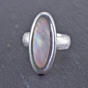 Könnte beinhalten: Ein silberner Ring mit einem ovalen, irisierenden Perlmuttstein, der in einer silbernen Fassung sitzt.