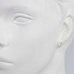 May include: A close-up of a mannequin's ear with a small silver bar earring.