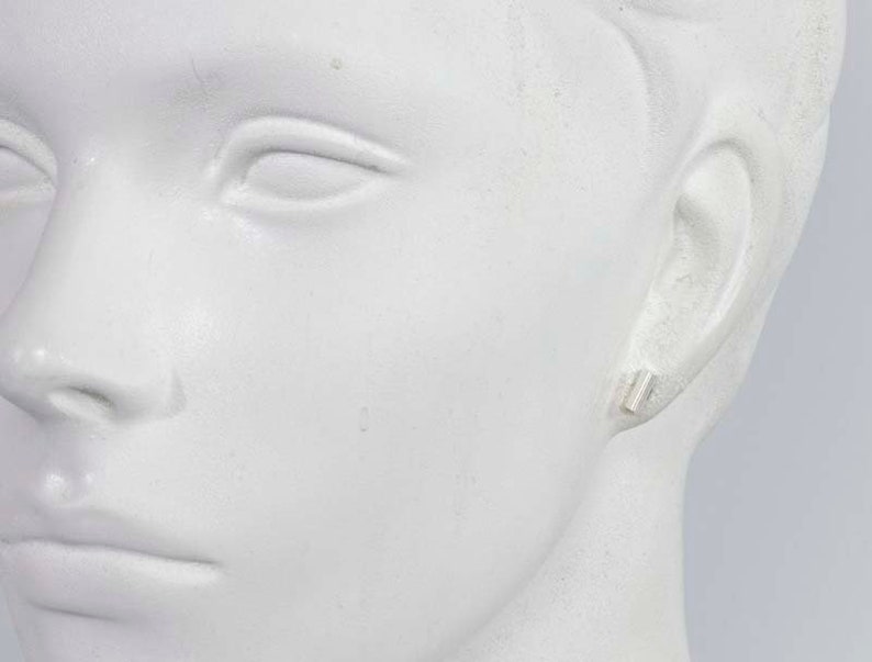 May include: A close-up of a mannequin's ear with a small silver bar earring.